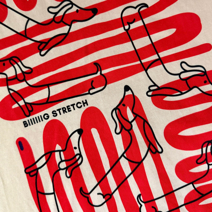 Close-up of a printed fabric featuring red and white horizontal stripes, black line drawings of dachshunds, and the text &