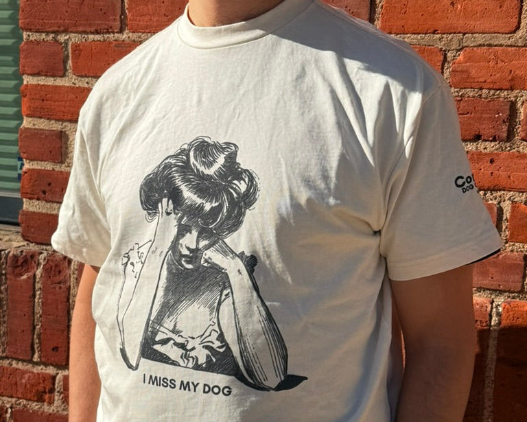 Person wearing a white t-shirt with a graphic design and text in front of a brick wall.