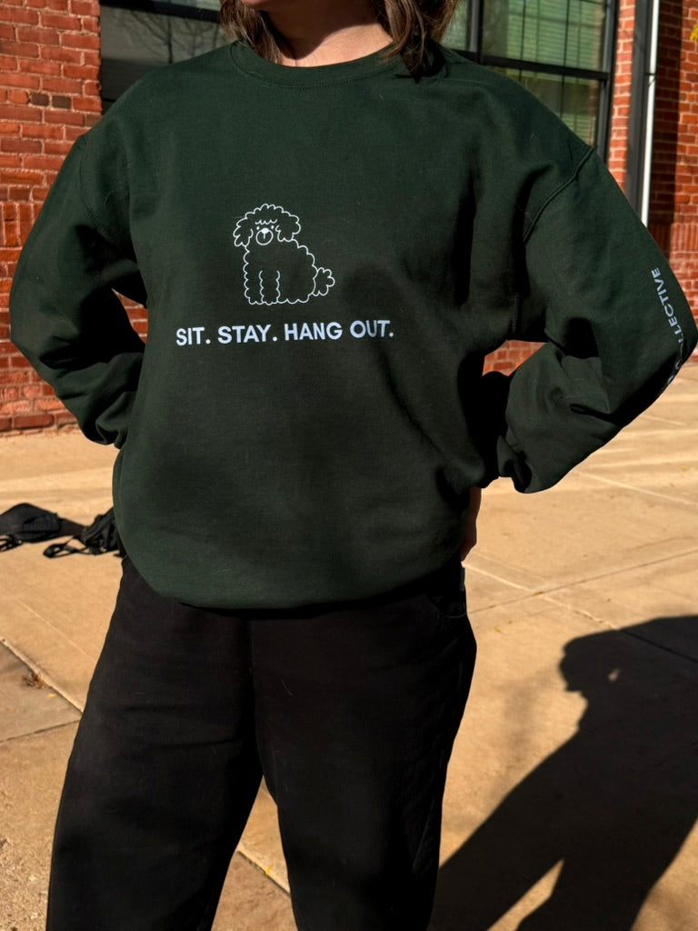 Person wearing a dark green sweatshirt with a dog graphic and text outdoors.