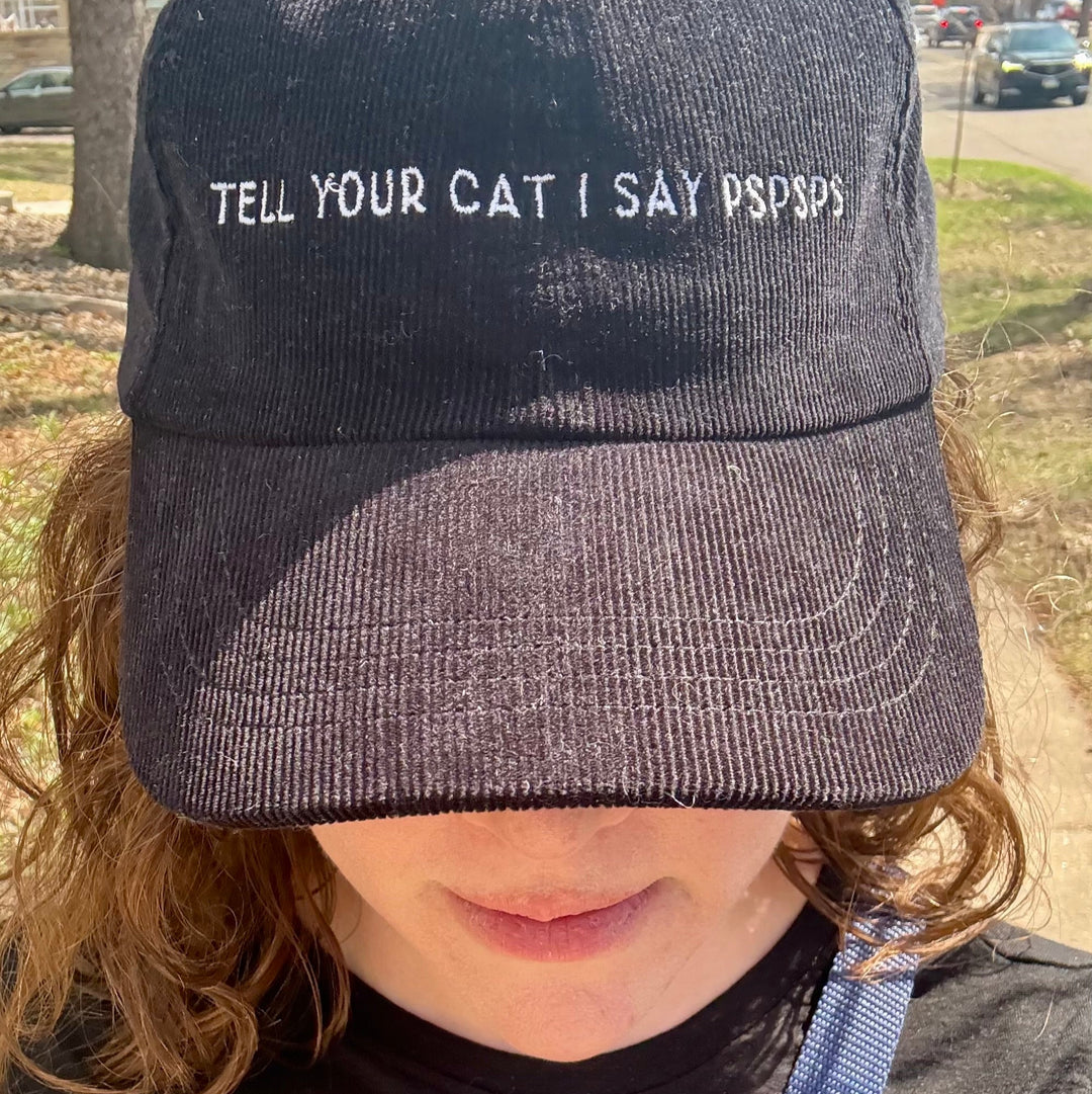 Woman wearing a baseball hat that says Tell Your Cat I Say Pspsps
