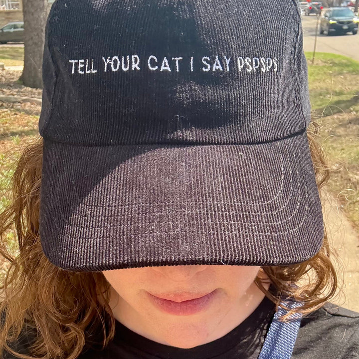 Woman wearing a baseball hat that says Tell Your Cat I Say Pspsps