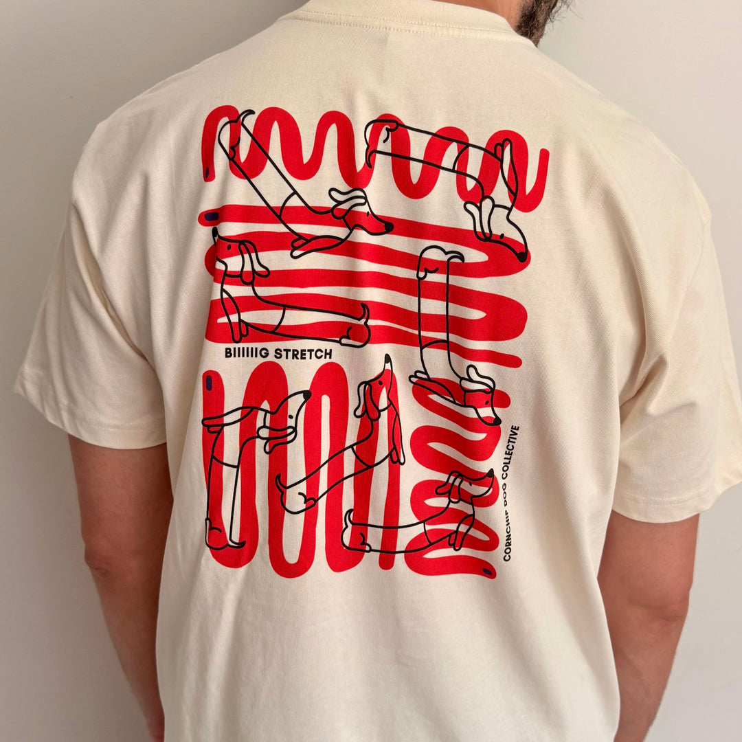 A person shown from the back wearing a cream-colored t-shirt with a large red and black graphic print on the back. The graphic features stylized dog illustrations and the text BIIIIG STRETCH 