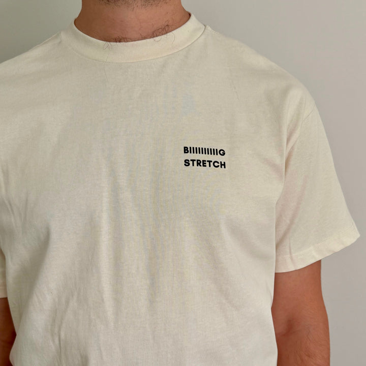A close-up of a person wearing a cream-colored short-sleeve t-shirt with the text &