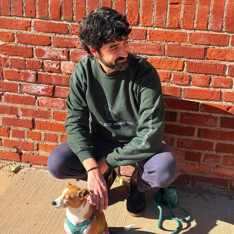 Man sitting on a sidewalk with a small dog in front of a brick wall